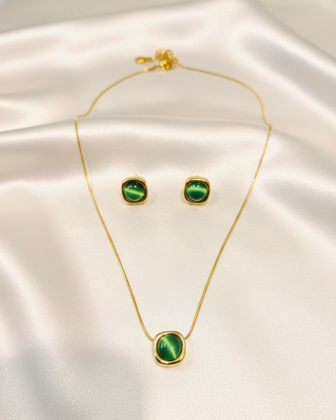 Gold necklace and earrings with green stones on a satin surface